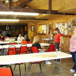 People seated and standing in a community hall with tables and chairs.