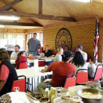 A man speaks to a group seated in a rustic meeting room.