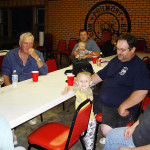 A family gathering around a table in a cozy room with red chairs.