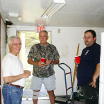 Three men working together in a basement with tools and gloves.