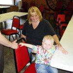 Woman and child holding hands in a room with tables and chairs.