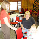 A woman handing a small package to a child while another woman watches.
