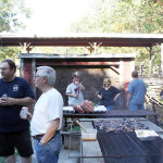 People grilling meat outdoors in a casual gathering.