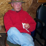Man in a red jacket and hat sitting on a chair indoors.