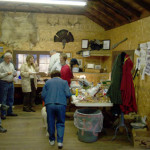 People gathered inside a rustic wooden room with food on a table.