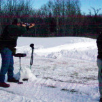 Two people shooting rifles outdoors in a snowy area.