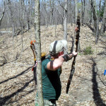 Person aiming a bow in a wooded area during fall or early spring.