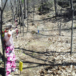 Person aiming with a handgun on a wooded outdoor shooting range.