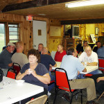 People gathered indoors, sitting and chatting around tables in a cozy setting.