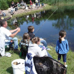 Family fishing by a peaceful pond on a sunny day.