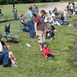 People gathered outdoors, watching an event on a sunny day.