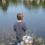 A boy fishing by the lake with a dog beside him.