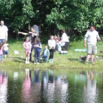 Families enjoying a sunny day by the pond, fishing and relaxing.
