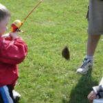 A child fishing with an adult on a grassy bank.