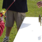 Child and adult fishing, holding a small fish caught.