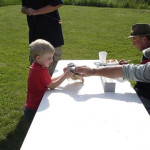 A child and an adult arm wrestling across a white table outdoors.