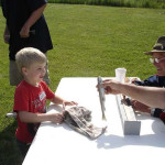 A young boy receiving a prize from a man at a table outdoors.