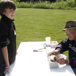 An elderly man signs a baseball for a young boy outdoors.