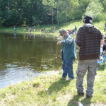 Children fishing by a calm river on a sunny day.