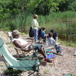 People fishing by a calm lakeside on a sunny day.