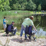 People enjoying fishing by a peaceful lakeside on a sunny day.