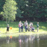 A group of people fishing by a peaceful lakeside surrounded by trees.