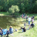 People fishing along a calm riverbank on a sunny day.