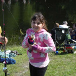 A young girl smiling while fishing by a pond.