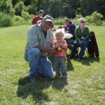 Man and toddler outdoors with family in background on sunny day.