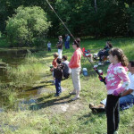 Children and adults enjoy a day fishing by a pond in a wooded area.