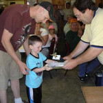 A young boy receives a trophy from an adult in a crowded room.