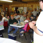 People gathered in a wooden hall, listening to a speaker.