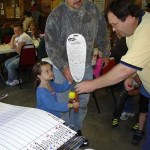 A child receives a balloon animal from an adult during a lively indoor event.