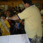 Man handing out items to children in a busy room.