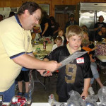 Man presenting a trophy to a boy at a crowded event.