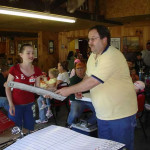 Man handing certificate to a young girl in a community hall.