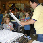 Man handing out papers to children in a classroom setting.