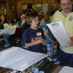 A boy looking at a man holding a menu in a busy indoor setting.
