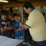 Man demonstrating a craft to children at a table indoors.