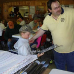 Man helping a child hold a fishing rod indoors.