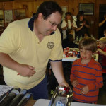 Man demonstrating a small steam engine to a curious boy.