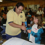 Man presenting a trophy to a young girl indoors.