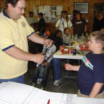 Man handing a trophy to a boy in a crowded room.