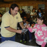 Man handing a trophy to a young girl in a busy room.