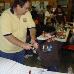 A man hands a trophy to a young boy in a busy room.