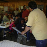 A man hands a rolled paper to a smiling boy in a lively indoor gathering.