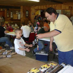 A man shows a young boy a model car at a hobby event.