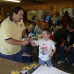 Man presenting a trophy to a young boy at an indoor event.