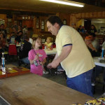 Man presenting a trophy to a young girl in a crowded hall.