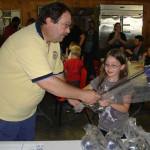 A man hands a toy sword to a smiling girl indoors.